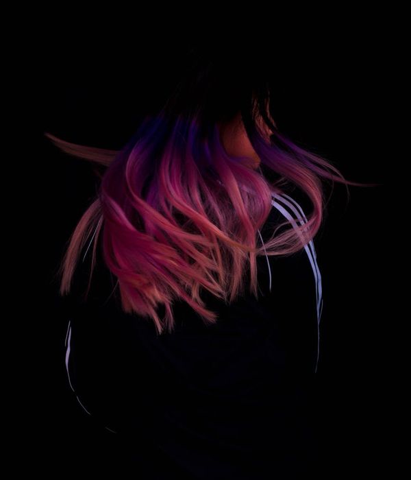 Woman performing a gentle, energetic movement in a dark studio with purple light accents.